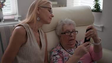 Bir kız, yaşlı annesine yaşlılar yurduna yaptığı bir ziyarette akıllı telefondan nasıl arama yapılacağını öğrenmesi için yardım ediyor..