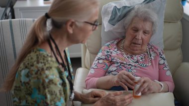 Neşeli bir hemşire, huzur ve refahını sağlamak için huzurevinde yaşlı bir kadının reçeteli ilaçlarını izlerken sohbet eder..