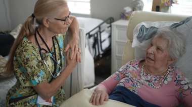 Huzurevinde, mutlu bir hemşire yaşlı bir kadının hayati organlarını kontrol ederken onunla sıcak bir konuşma yapar, iletişim kurar ve ilgilenir..