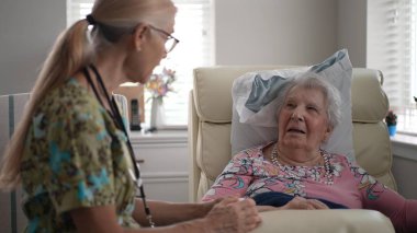 Huzurevindeki yaşlı bir kadını ziyaret eden bir hemşire, sağlık ve günlük hayatı hakkında keyifli bir konuşma yaparken hayati organlarını kontrol ediyor..