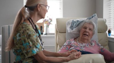 Bir hemşire yaşlı bir kadının elini tutarken onu huzur evinde dostça bir sohbete sokuyor. İkisi de mutlu ve nişanlı görünüyor..