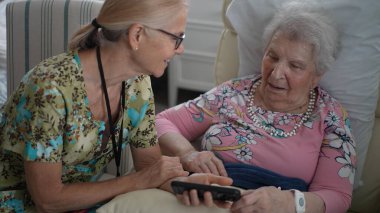 Mutlu hemşire yaşlı bir kadınla konuşuyor, sıcak ve davetkar bir ortamda huzur evini ziyaret ederken anılarını ve bilgilerini telefonla paylaşıyor..