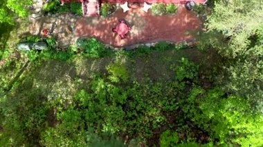 Ağaçların arasından inen hava manzarası, kayalık duvar bahçeleri ve tuğla kaplama ile tamamlanmış veranda alanını gösteriyor..