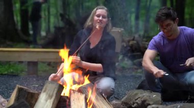 Oğlan bıçakla sopa yontuyor ve kız ateşte şekerleme pişiriyor..