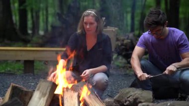 Kamera sağa sola kayıyor. Genç bir çocuk sopayı bıçakla yontuyor ve bir kız ateşte şekerleme pişiriyor..