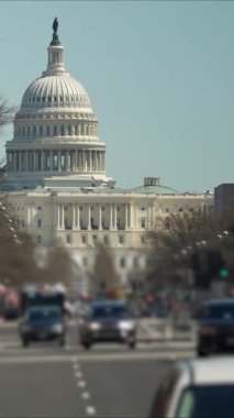 ABD Kongre Binası 'nın dikey videosu açık mavi gökyüzünün altında duruyor. Arabalar caddelerde geziniyor ve bayraklar bölgeyi süslüyor, hareketli bir atmosfer yaratıyor..