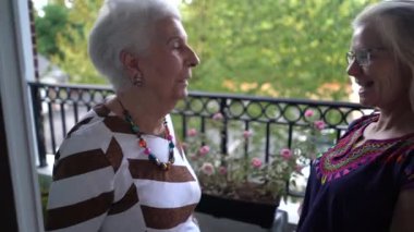 Gülümserken, yaşlı bir kadın ve genç bir kadın balkonda birbirlerine sarılıyorlar..