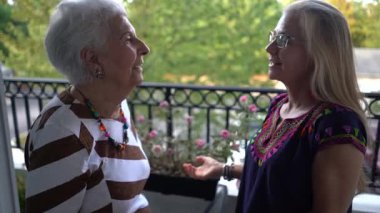 Gülerken, yaşlı bir kadın ve genç bir kadın balkonda birbirlerine sarılıyorlar..