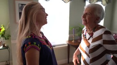 Gülerken, yaşlı bir kadın ve genç bir kadın yemek odasında sarılıyorlar..