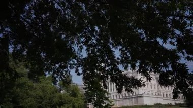 Açık mavi gökyüzü ile güneşli bir günde, Washington, DC 'deki hükümet merkezi olan ABD Kongre Binası' nın ağaçlarının arasından manzarayı seyret..