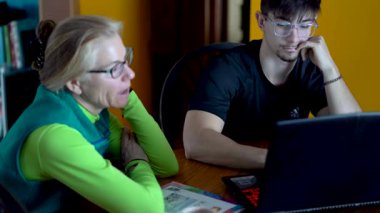 Anne ve oğlu yemek masasında ödevlerini yaparken oğlu dizüstü bilgisayarda yazı yazıyor..