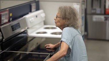 Son sınıf öğrencisi bir kadın, bir hırdavatçıdan ev dekorasyonu malzemeleri alırken yürüteç kullanıyor. Çeşitli alet ve eşyaları dikkatlice inceliyor..