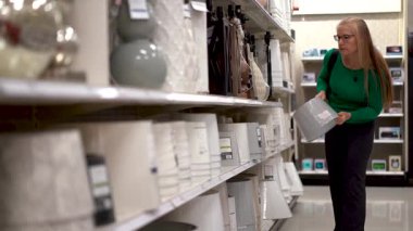 Güzel, sarışın, olgun bir kadının, alışveriş merkezindeki abajur ve lambalara bakarken geniş açılı görüntüsü..