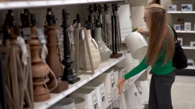 Güzel, sarışın, olgun bir kadın vitrindeki abajurları inceliyor..