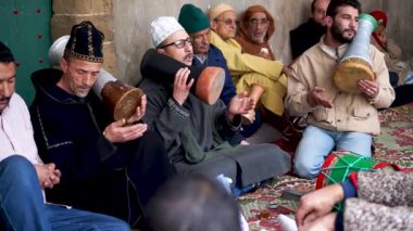 Geleneksel giyinmiş bir grup kadın ve erkek sufi töreninde şarkı söyleyip davul çalıyorlar..