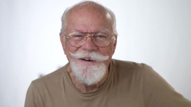 Yakışıklı, yaşlı bir adamın, beyaz arka planda kameraya bakarken gülümseyen portresi. İnsan duyguları ve yüz ifadeleri 