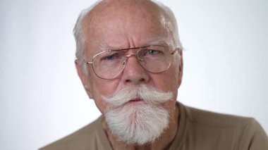 Yakın plan, yaşlı bir adamın sağlam beyaz arka planda kameraya bakarken çekilmiş ciddi bir portresi..