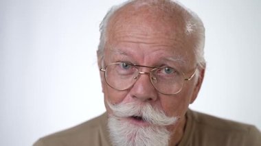 Yakışıklı, yaşlı bir adamın, beyaz arka planda kameraya bakarken gülümseyen portresi. İnsan duyguları ve yüz ifadeleri 