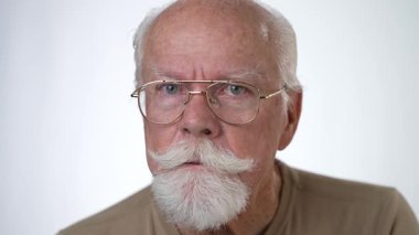 Yakın plan, yaşlı bir adamın sağlam beyaz arka planda kameraya bakarken çekilmiş ciddi bir portresi..