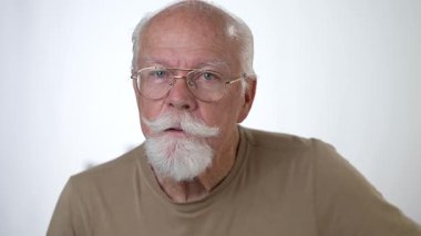 Yakın plan, yaşlı bir adamın sağlam beyaz arka planda kameraya bakarken çekilmiş ciddi bir portresi..