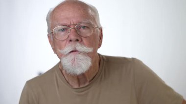 Yakın plan, yaşlı bir adamın sağlam beyaz arka planda kameraya bakarken çekilmiş ciddi bir portresi..