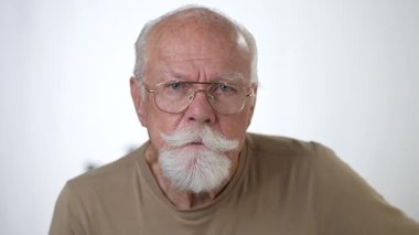 Yakın plan, yaşlı bir adamın sağlam beyaz arka planda kameraya bakarken çekilmiş ciddi bir portresi..
