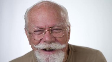 Yakışıklı, yaşlı bir adamın, beyaz arka planda kameraya bakıp gülen portresi. İnsan duyguları ve yüz ifadeleri 