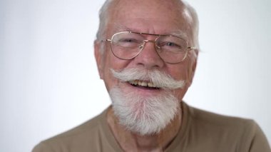 Yakışıklı, yaşlı bir adamın, beyaz arka planda kameraya bakarken gülümseyen portresi. İnsan duyguları ve yüz ifadeleri 