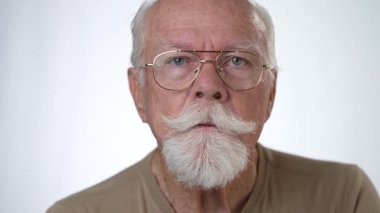 Yakın plan, yaşlı bir adamın sağlam beyaz arka planda kameraya bakarken çekilmiş ciddi bir portresi..