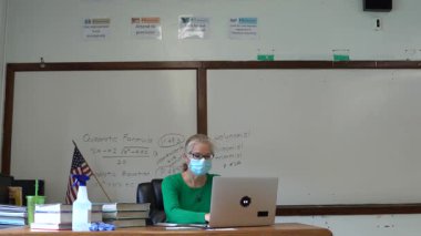 Masada çalışan öğretmen, masa başında tıbbi maske takıyor ve masa başında PPE ve ABD bayrağı var..