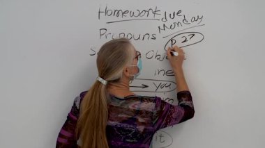 Bir okul sınıfında beyaz tahtaya yaslanmış gülümseyen olgun bir İngilizce dil bilgisi öğretmeninin aşırı yakın portresi..