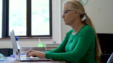 Okuldaki öğretmenlerin masadaki bilgisayarda tıbbi yüz maskesi ve masasında PPE ve ABD bayrağı olan dezenfektanlarla yakın çekim görüntüleri..