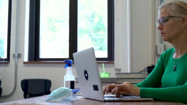 Okuldaki öğretmenlerin masadaki bilgisayarda tıbbi yüz maskesi ve masasında PPE ve ABD bayrağı olan dezenfektanlarla yakın çekim görüntüleri..