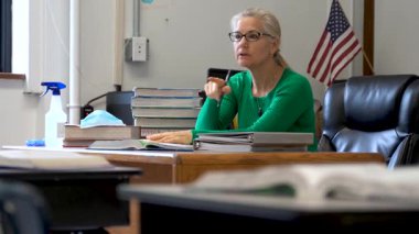 Masasında sağlık maskesi ve dezenfektanla çalışan öğretmen masada PPE ve ABD bayrağı arkasında..