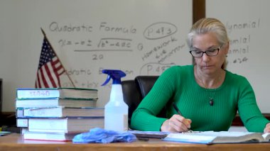 Masada çalışan, tıbbi maske takan ve masa başında PPE ve ABD bayrağı taşıyan öğretmenlerin yakınlaşması..