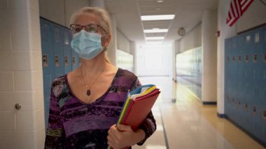 Boş bir okulda, elinde boş bir kitapla, elinde maskeyle, koridorda yürüyen öğretmenin yavaş çekim ön görüntüsü..