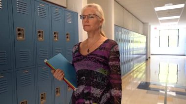 Öğretmenin boş bir okulda koridorda yürürken elinde boşluğu gösteren kitaplarla ağır çekim ön görüntüsü..