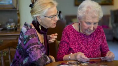 Yaşlı kadın kızıyla fotoğraflara bakıyor. Kıdemli kadın yemek odasında oturmuş kızıyla fotoğraflarına bakıyor. Beyin eğitimi. Bellek etkinliği.