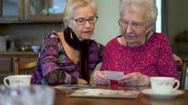Yaşlı ve gülümseyen bir kadının eski fotoğraflara bakıp yemek masasında kızıyla olan anılarını hatırladığı yakın plan..