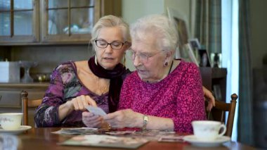Yaşlı, gülümseyen, mutlu bir kadın eski fotoğraflara bakıyor ve yemek masasındaki kızımızla ilgili anıları hatırlıyor..