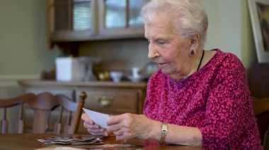 Yaşlı, yaşlı, mutlu bir kadın, masada oturmuş fotoğraf hatıralarına bakıyor..