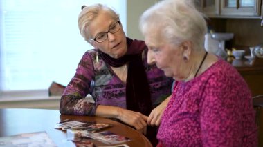Yaşlı yaşlı kadın eski fotoğraflara bakıyor ve yemek masasında kızıyla anılarını hatırlıyor..