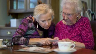 Yaşlı bir kadının eski fotoğraflara bakıp kızıyla yemek masasında geçirdiği anıları hatırladığı son derece yakın plan..
