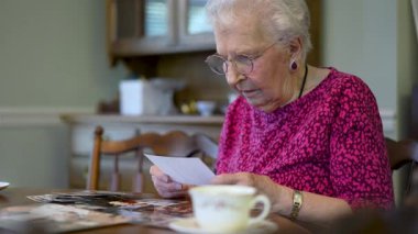 Yaşlı, gülümseyen bir kadının eski fotoğraflara baktığı ve kızının yemek masasında ona katıldığı anıları hatırladığı son derece yakın plan..