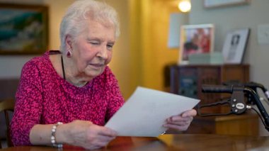 Yaşlı, yaşlı, mutlu bir kadın, masada oturmuş fotoğraf hatıralarına bakıyor..