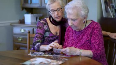 Yaşlı yaşlı kadın eski fotoğraflara bakıyor ve yemek masasında kızıyla anılarını hatırlıyor..