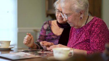 Yaşlı bir kadının eski fotoğraflara bakıp kızıyla yemek masasında geçirdiği anıları hatırladığı son derece yakın plan..