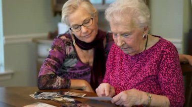 Yaşlı kadın kızıyla fotoğraflara bakıyor. Kıdemli kadın yemek odasında oturmuş kızıyla fotoğraflarına bakıyor. Beyin eğitimi. Bellek etkinliği.