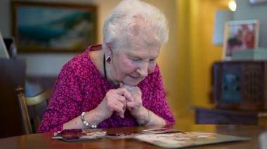 Yaşlı yaşlı bir kadın gülümsüyor ve masada oturmuş fotoğraf hatıralarına bakıyor..