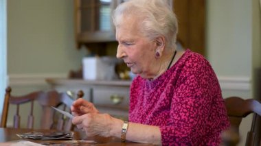 Yaşlı, yaşlı, mutlu bir kadın, masada oturmuş fotoğraf hatıralarına bakıyor..